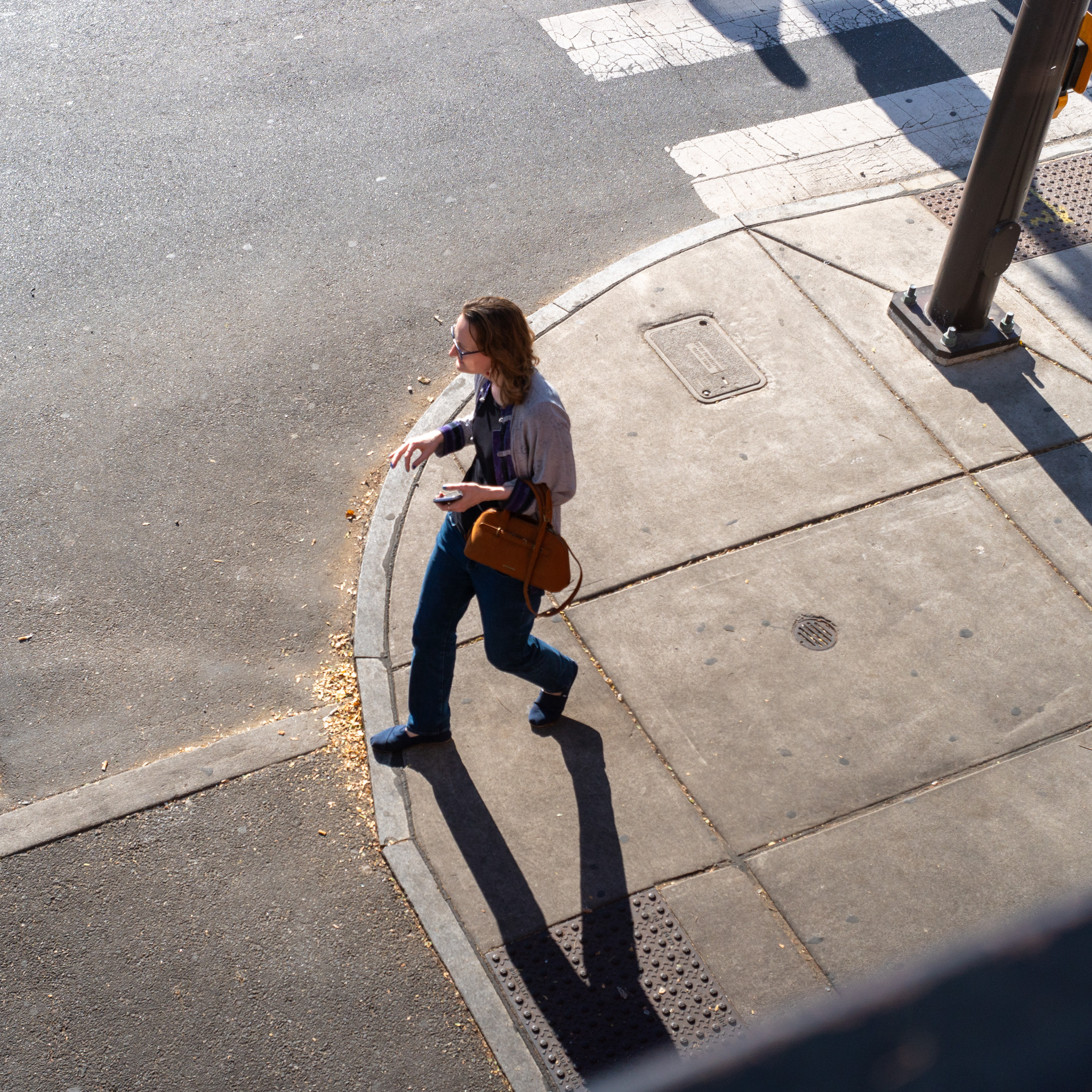 People seen from above at a corner in Manayunk, long afternoon shadows cast across the sidewalk.