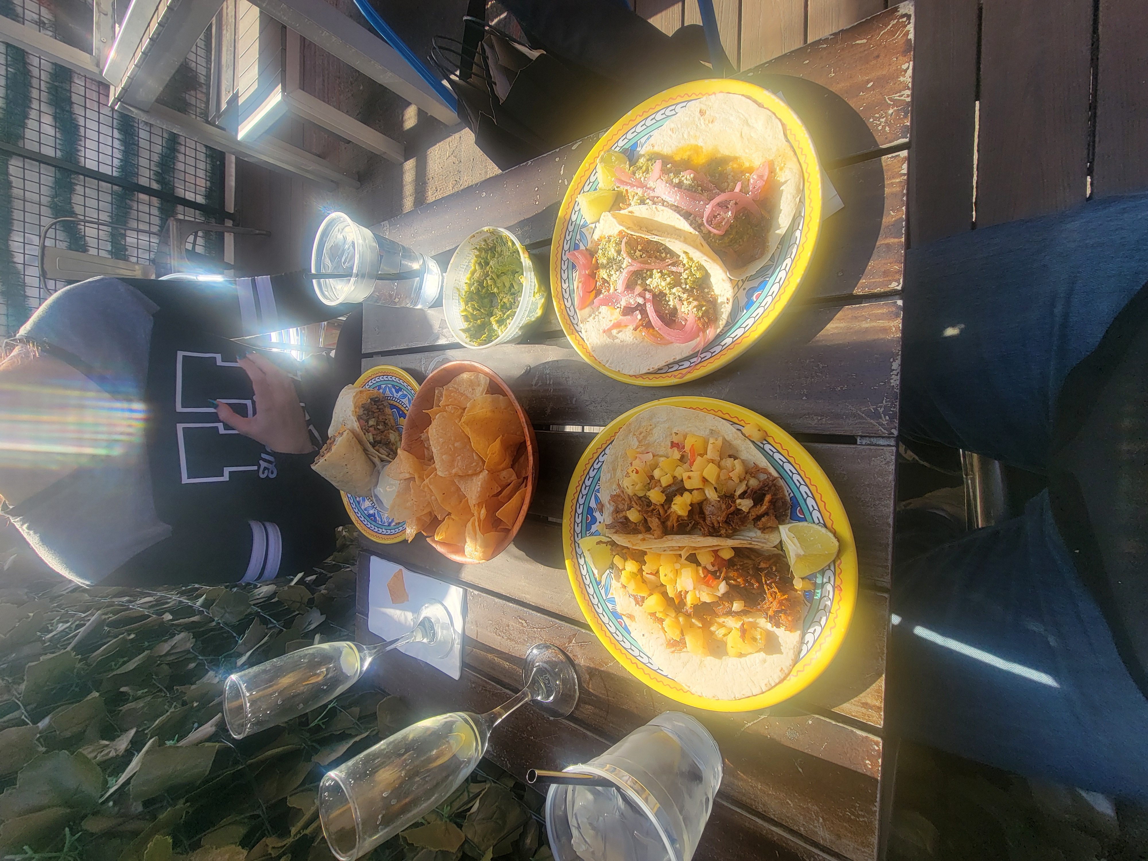 Two colorful plates of tacos with chips and guacamole on a wooden rooftop table.