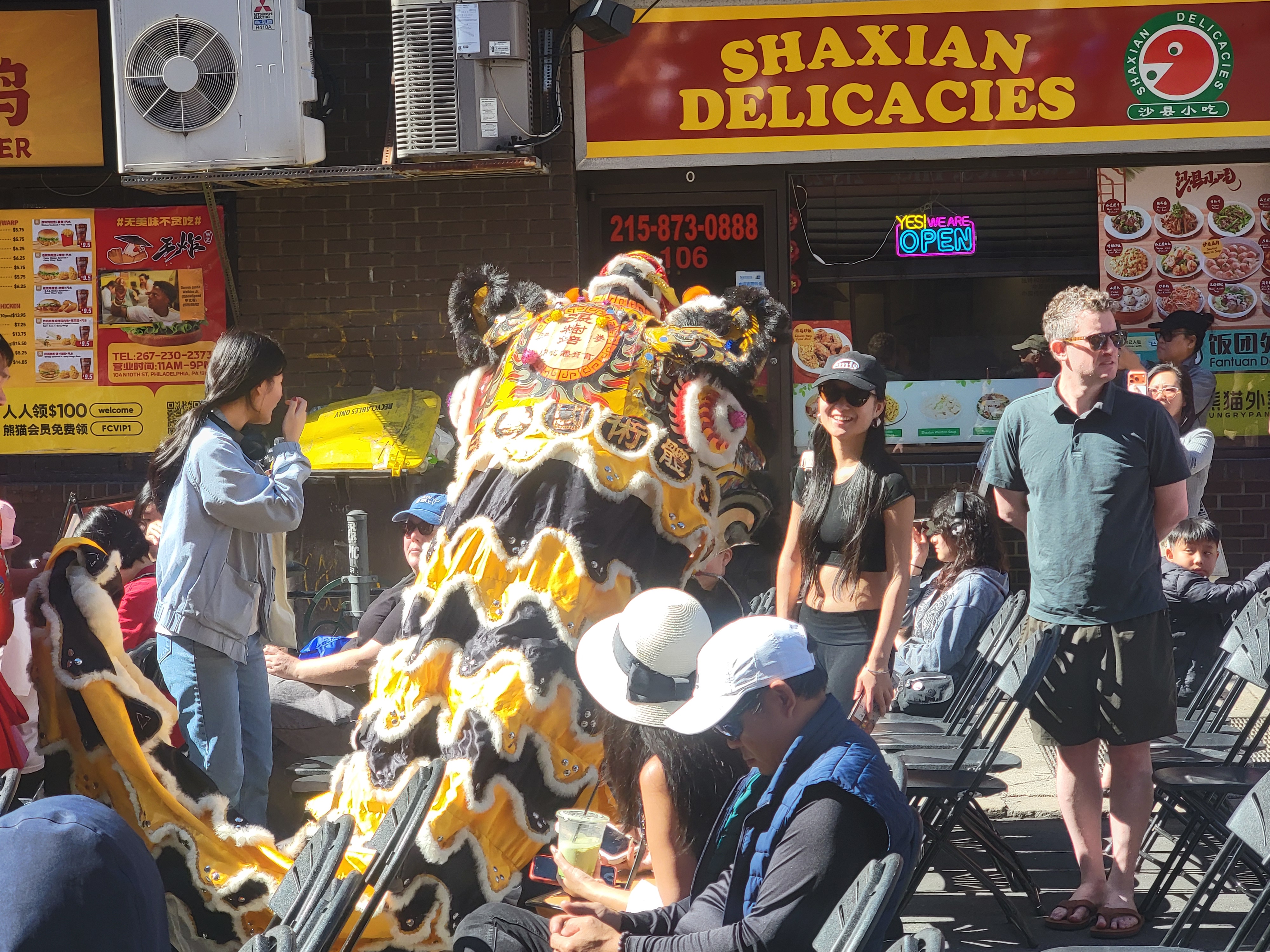 Lion dance weaving through chairs outside Shaxian Delicacies during the Chinatown Autumn Festival.